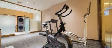 A modern fitness room with a stationary bike, a treadmill, and a wall-mounted elliptical.