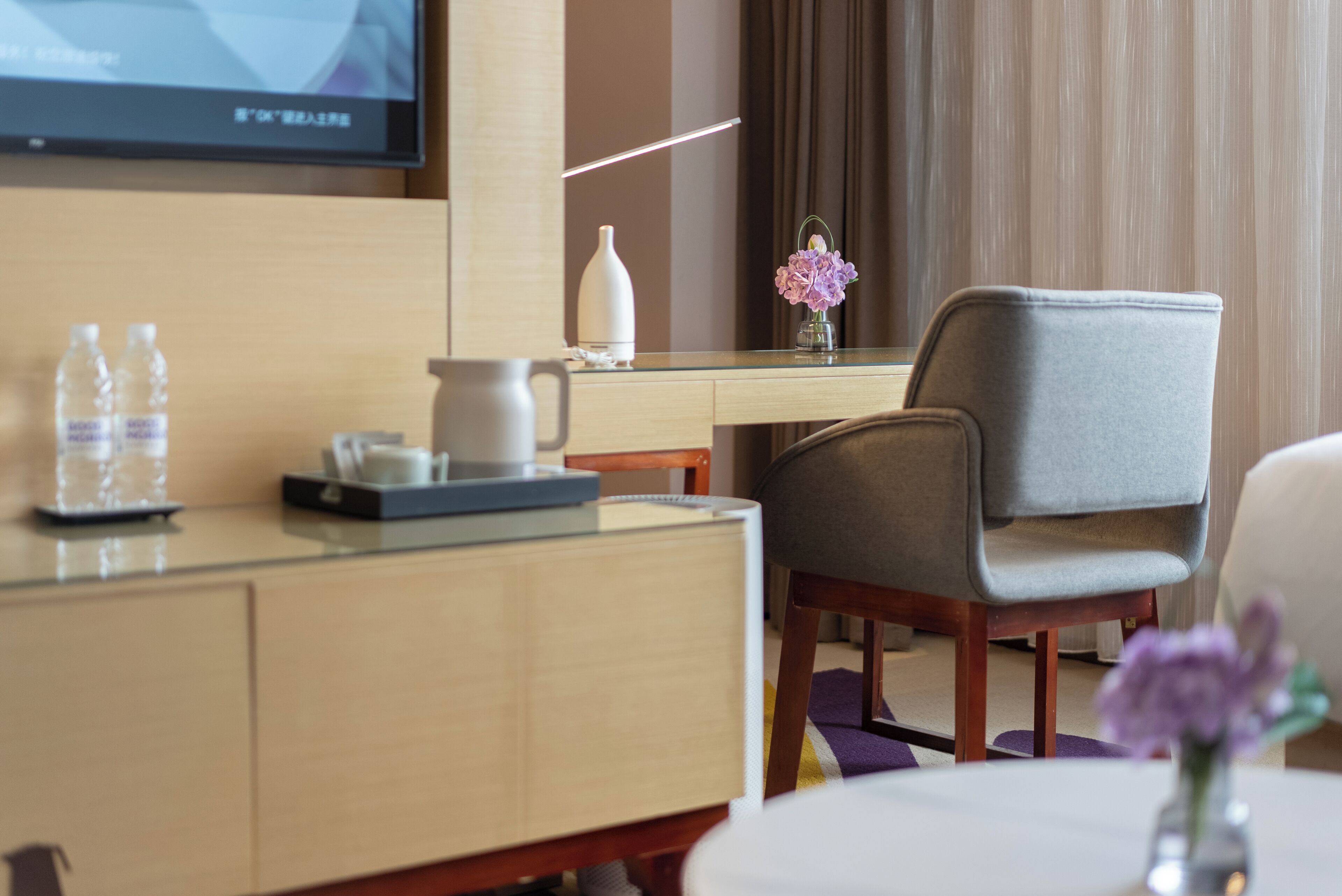 Habitación de hotel con escritorio de madera, una silla, un jarrón con flores, televisor y una cama.