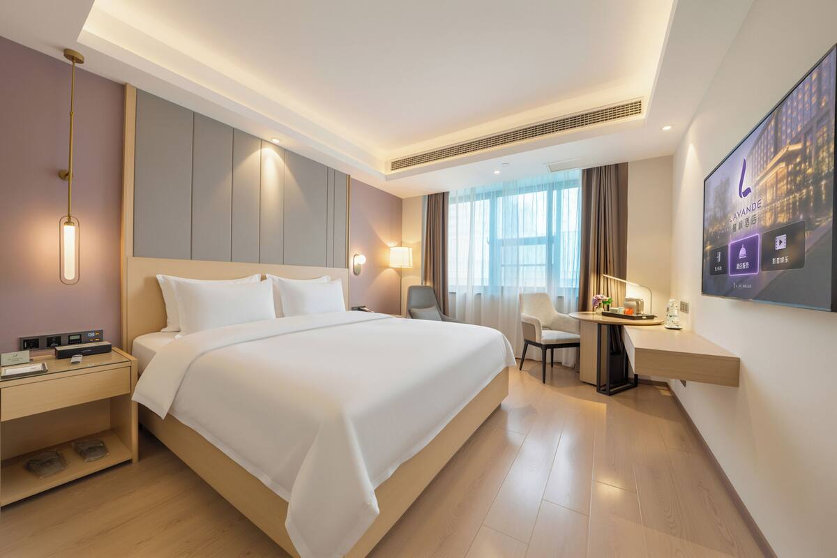 A hotel room with a large bed, bedside tables, a desk, a chair, and a TV screen.