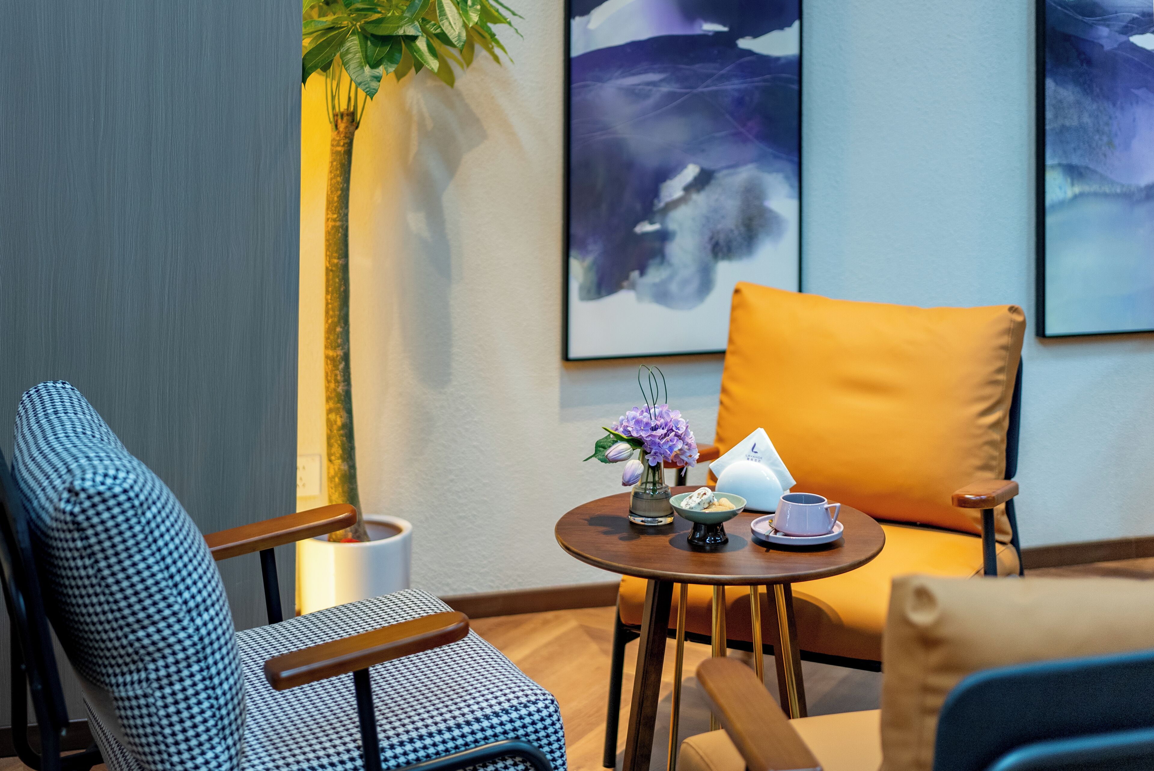 A cozy seating area with patterned chairs, a small round table with a teapot and cups, and a vase with flowers.