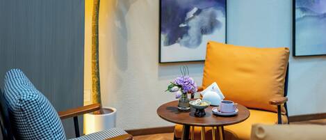 A cozy seating area with patterned chairs, a small round table with a teapot and cups, and a vase with flowers.