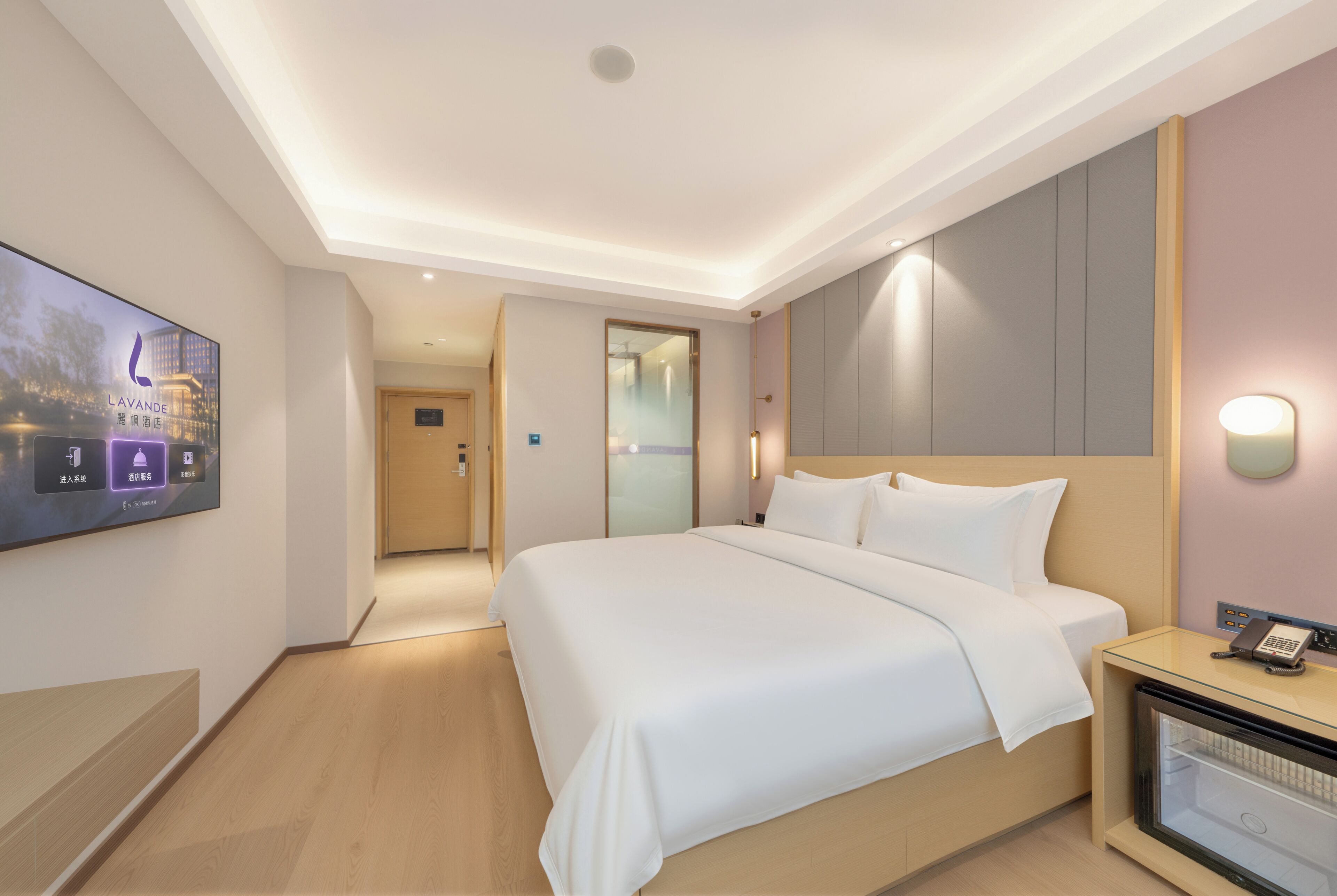 A hotel room with a bed, a TV mounted on the wall, a bedside table with a phone, and a glass cabinet.