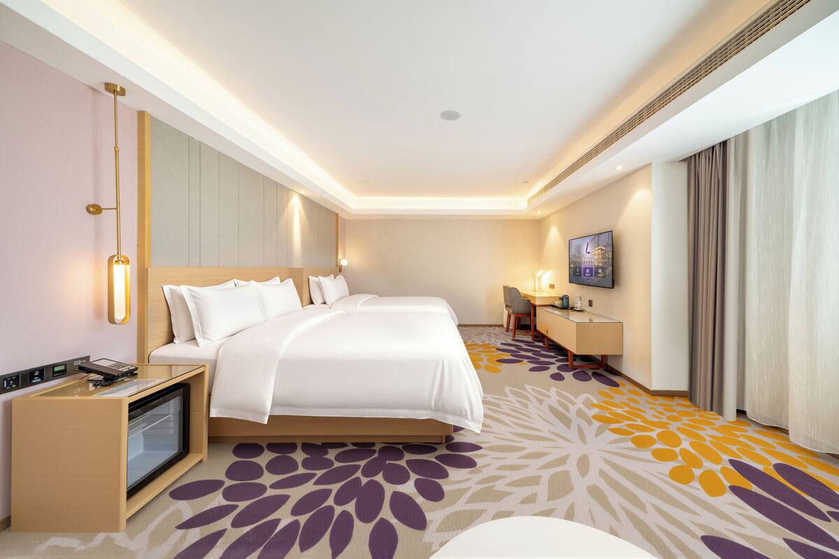 A hotel room with a bed, bedside table, TV, desk, and a patterned carpet.
