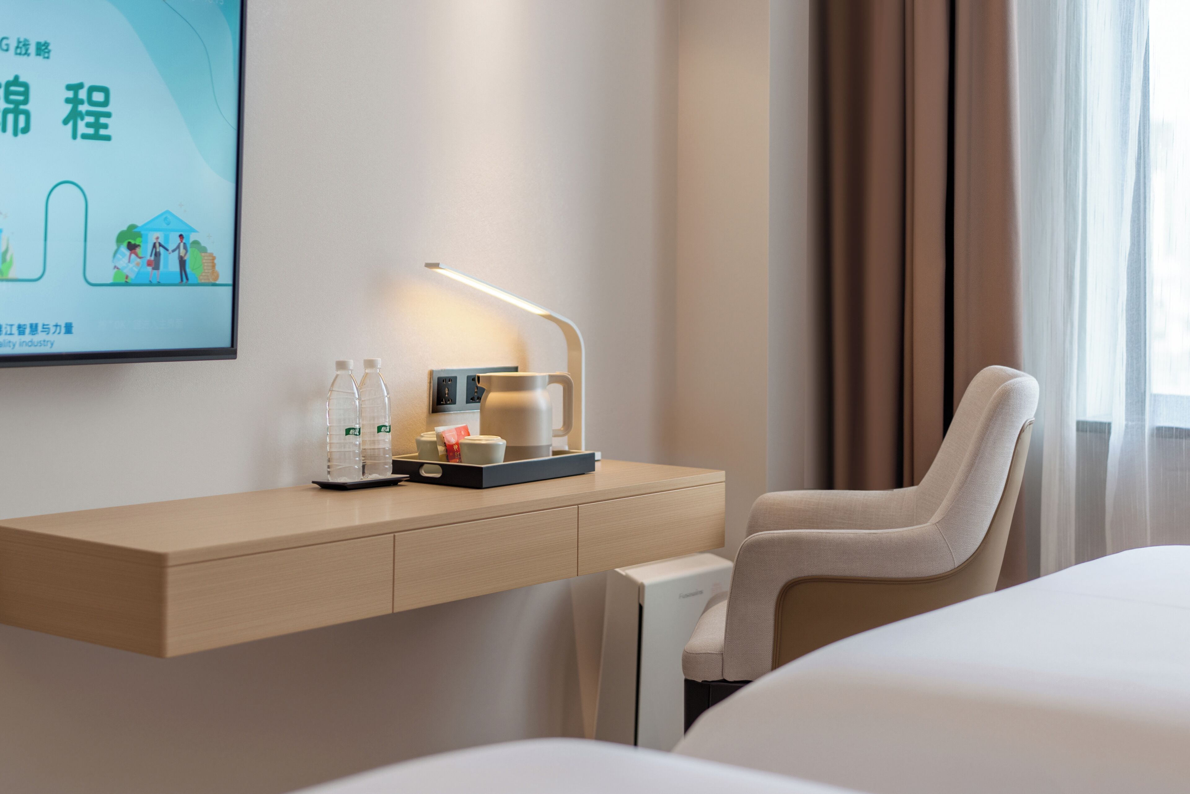 Une chambre d’hôtel équipée d’un bureau, d’une chaise, d’un lit, d’un téléviseur fixé au mur et d’une fenêtre avec des rideaux.