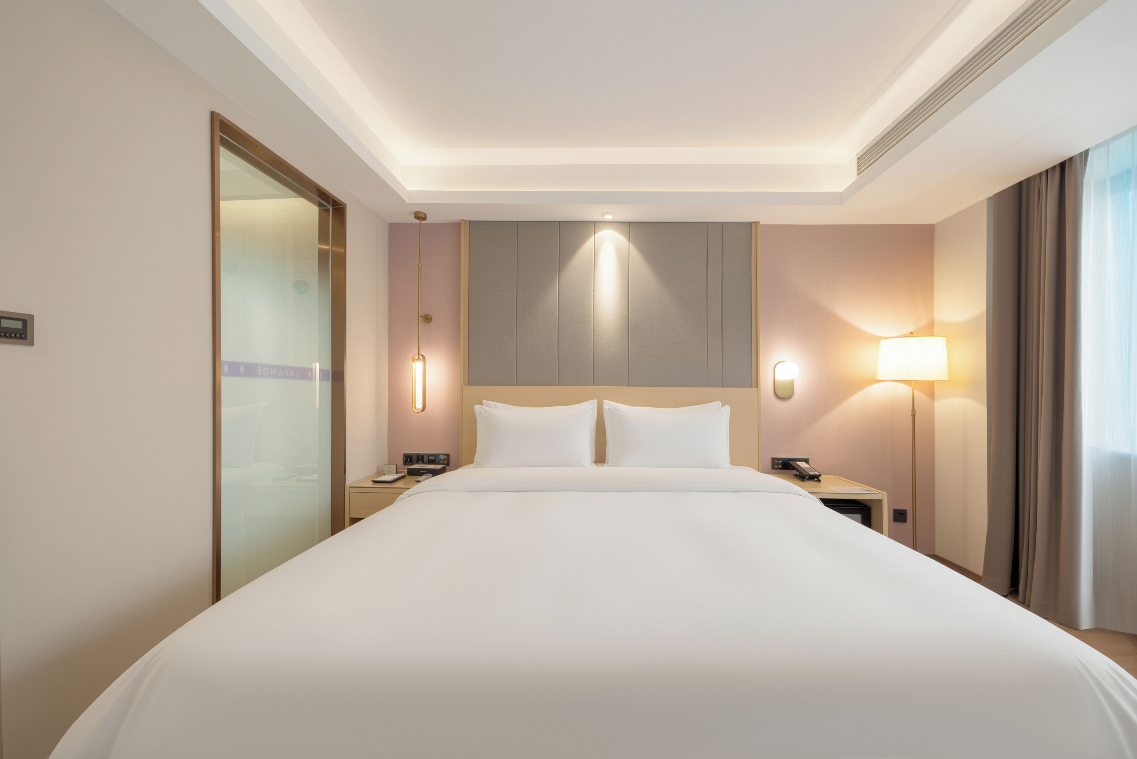 A hotel room with a large bed, bedside tables, a nightstand, a wall-mounted lamp, and a door with a frosted glass panel.