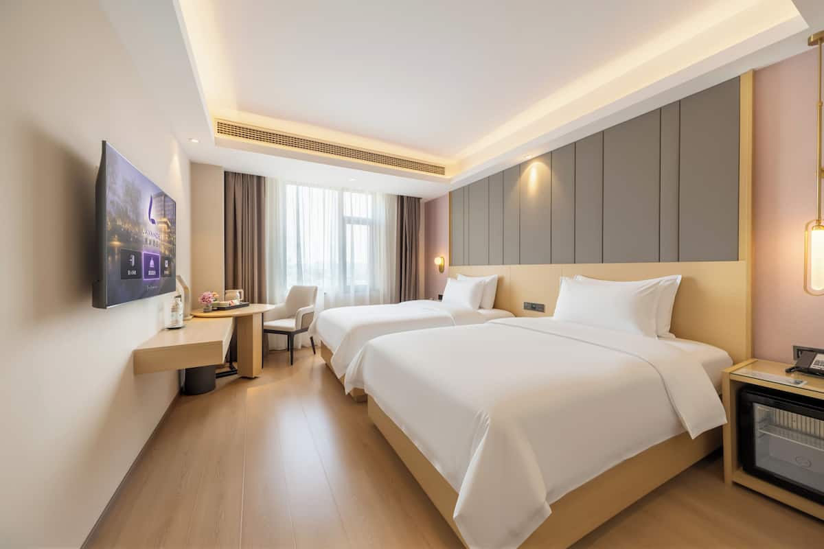 A hotel room with two beds, a desk, a chair, a TV, and a minibar.