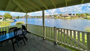A covered outdoor area with a view of a lake and houses in the background. - Bungalow in Holland by Water With Sauna (Simonshaven)