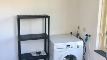 A compact laundry room with a Bosch washing machine, a black metal shelf, and a power outlet.