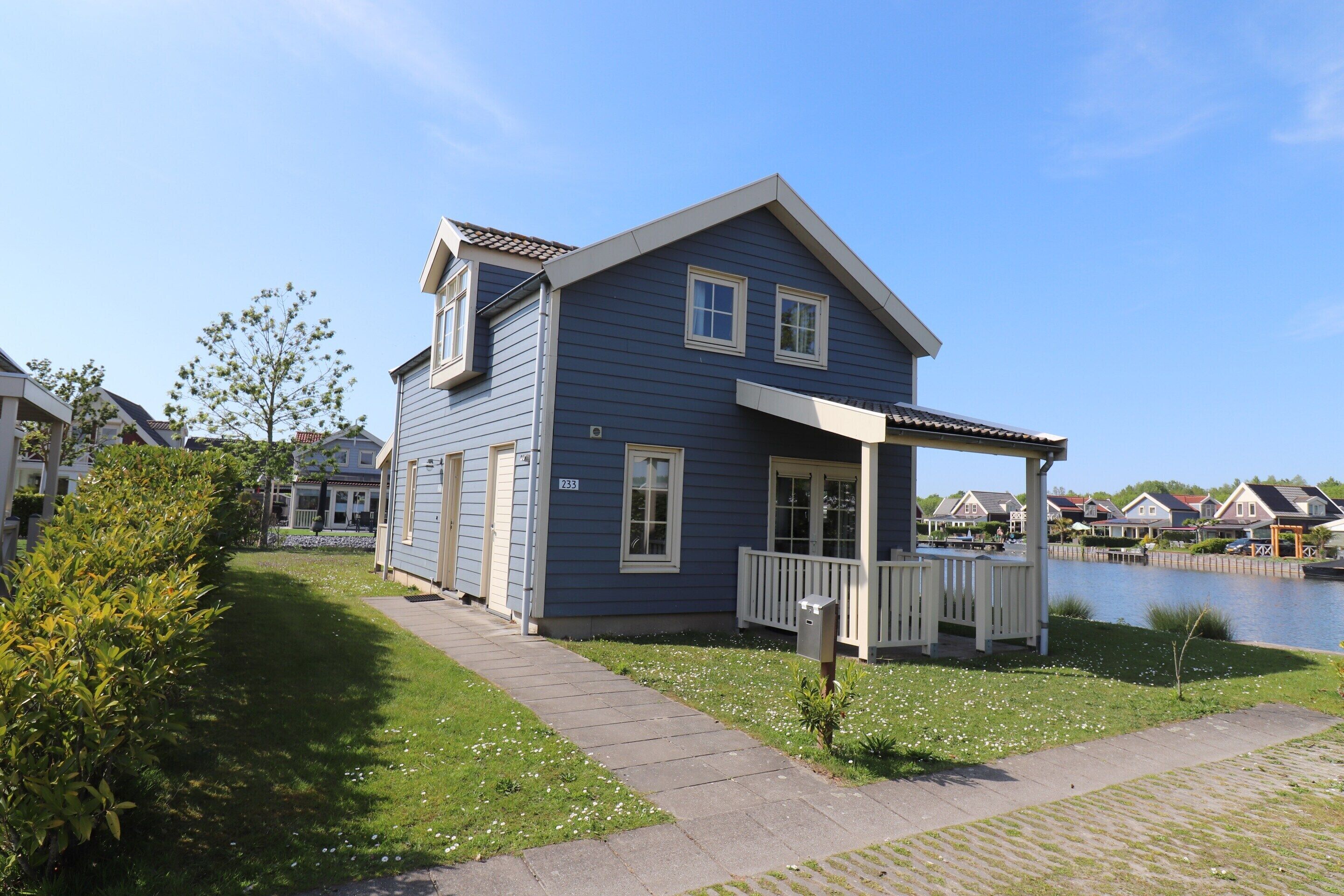 A blue house with a porch, a small garden, and a body of water in the background.