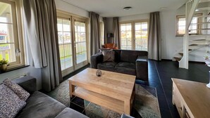A modern living room with a sofa, a coffee table, and a staircase. - Bungalow in Holland by Water With Sauna (Simonshaven)
