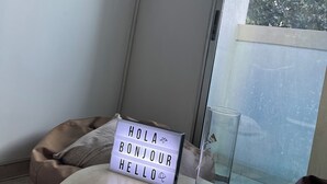 Una pequeña mesa con un letrero luminoso que dice "HOLA BONJOUR HELLO" y un florero de vidrio transparente.