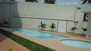 Una piscina con una sección curva, rodeada por un muro de ladrillo bajo y pequeñas palmeras.