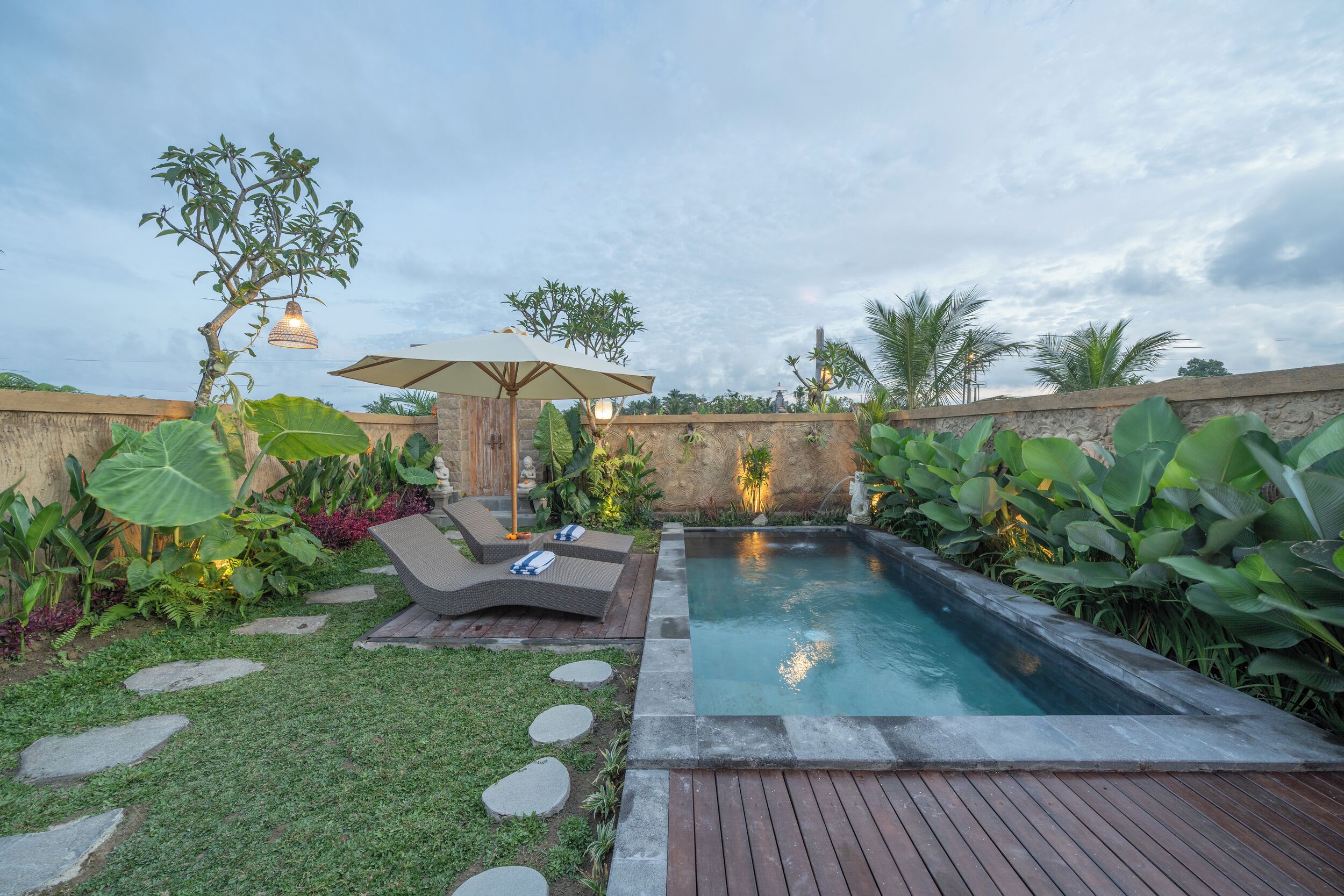 A backyard with a swimming pool, lounge chairs, and a pergola with hanging lights.