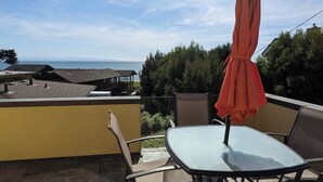 Un patio con una mesa, sillas y una sombrilla, con vista al mar y edificios al fondo.