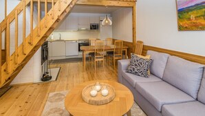 Un appartement moderne doté d’un escalier en bois menant à une chambre en mezzanine, d’un coin repas avec des meubles en bois et d’un salon comprenant un canapé et un tableau au mur.