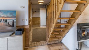 Un escalier en bois mène à une chambre aménagée en mezzanine, dotée d’une cheminée.