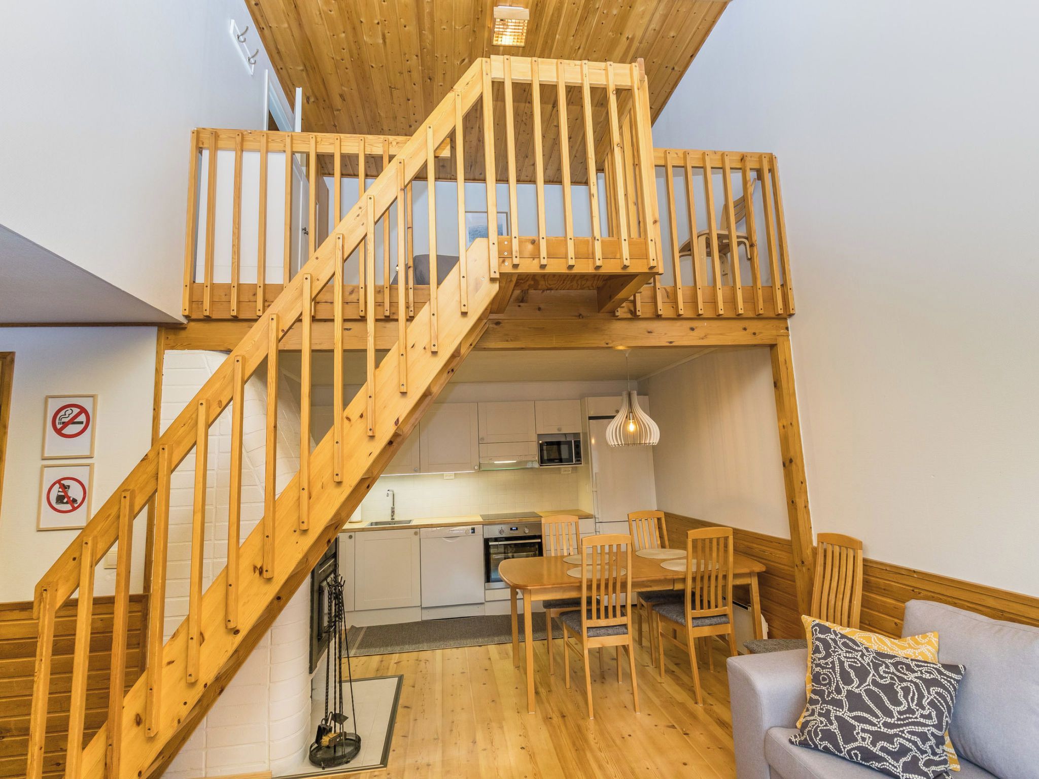 Un appartement de style « loft » avec un escalier en bois menant à une mezzanine, une cuisine équipée d’appareils électroménagers modernes et un coin repas avec des meubles en bois.