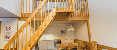 Een loft-appartement met een houten trap naar een entresol, een keuken met moderne apparatuur en een eethoek met houten meubels.