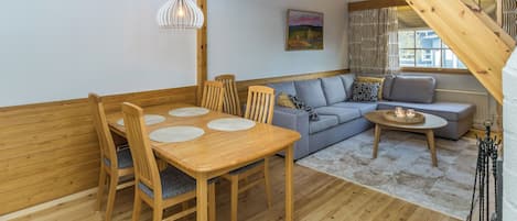 A cozy interior with a wooden dining table, chairs, a sofa, and a staircase.