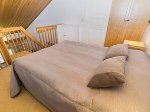 Un dormitorio con una cama grande, cabecera de madera, armario blanco y una escalera de madera.