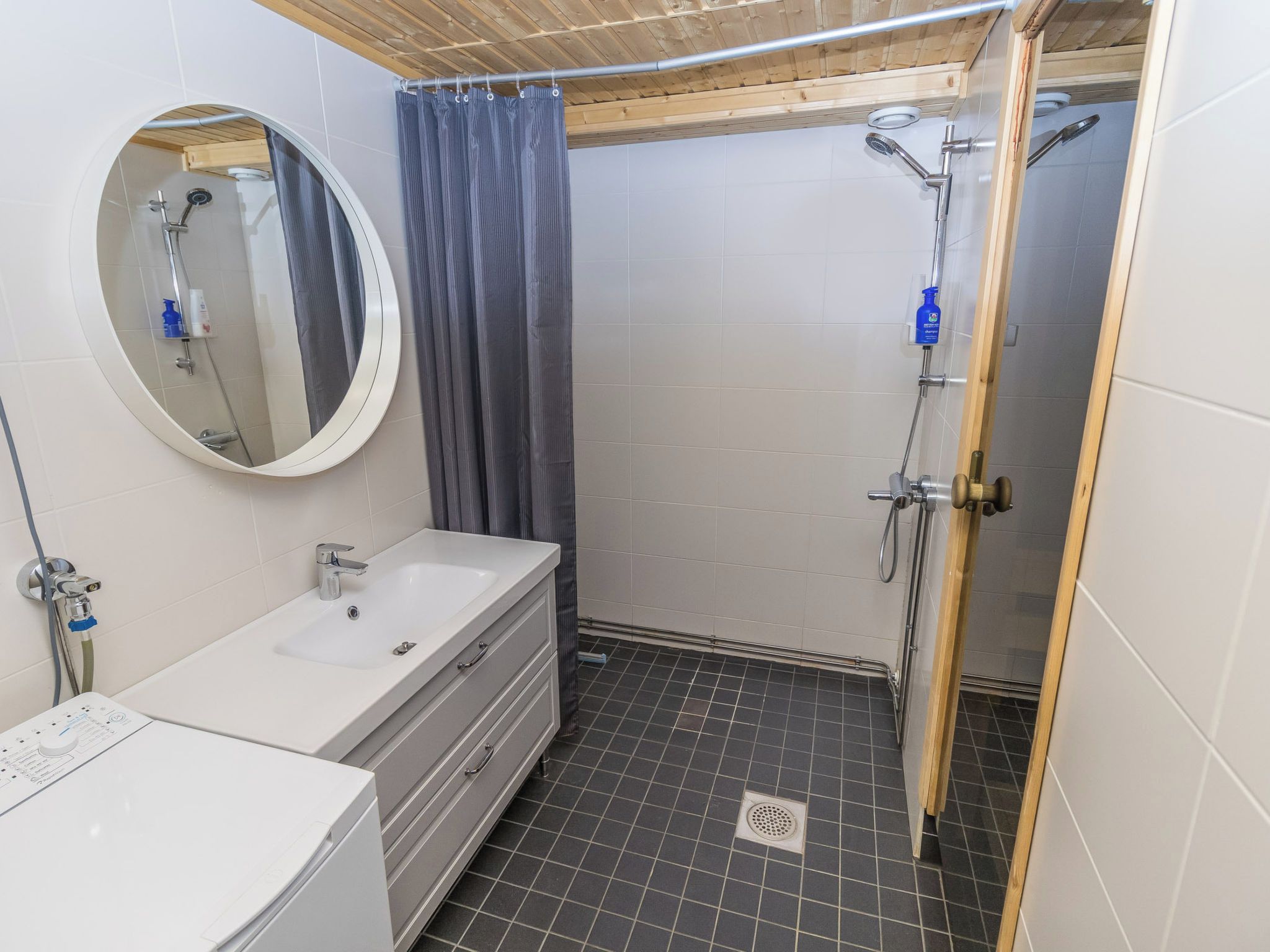 Een badkamer met een witte wastafel, een spiegel, een douche en een houten plafond.