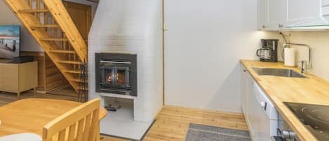 Une cuisine compacte dotée d’un poêle à bois, d’un plancher en bois et d’un petit coin repas avec une chaise.
