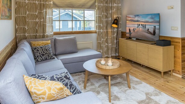 Un salon moderne avec un canapé d’angle gris, un meuble en bois et un téléviseur posé sur un support en bois.