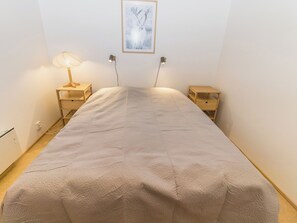 A bedroom with a bed, two bedside tables, a wall-mounted lamp, and a framed picture.