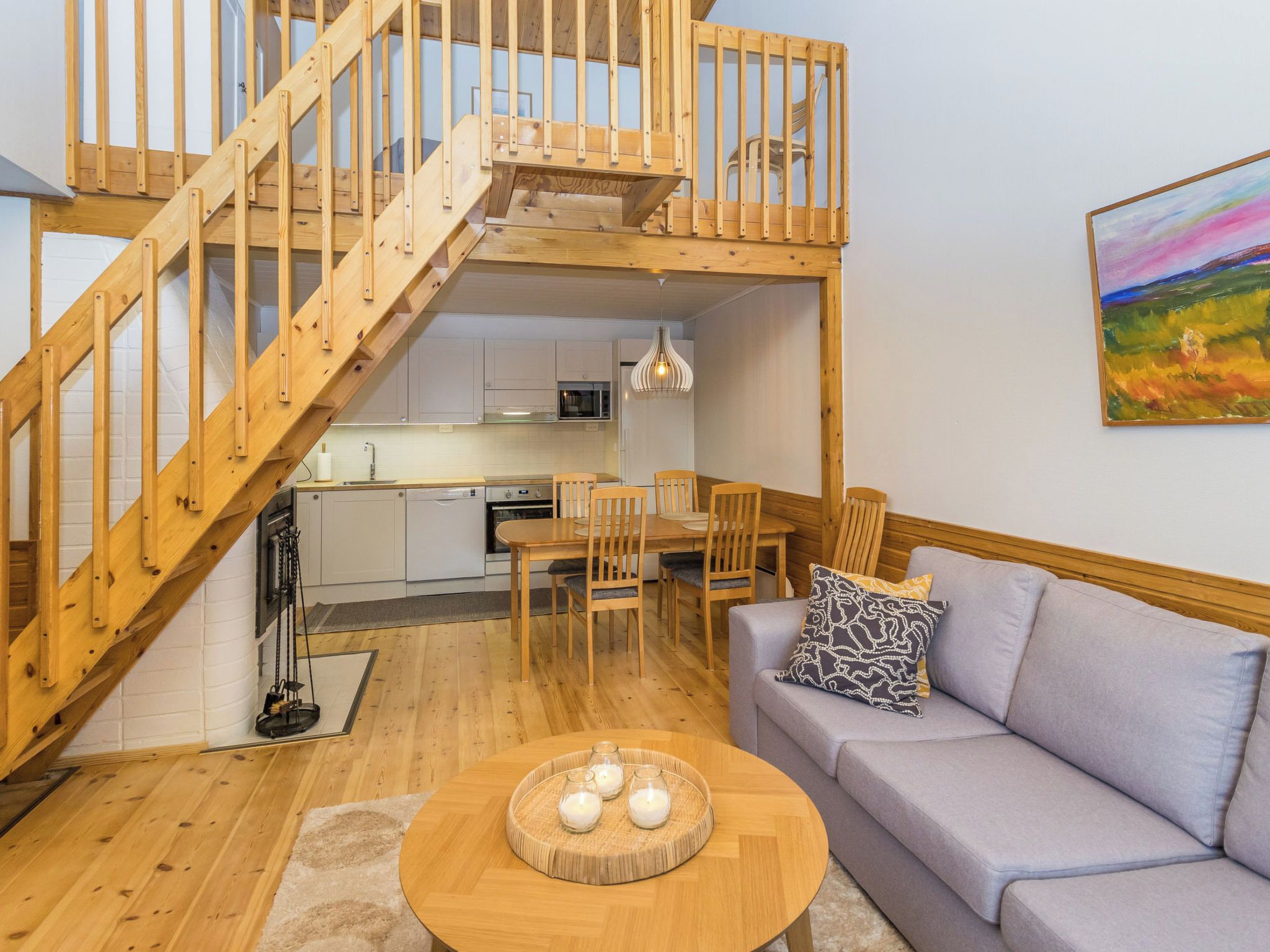 A modern apartment with a wooden staircase leading to an upper level, a kitchen with white cabinets, a dining area with a table and chairs, and a living room with a sofa and a coffee table.