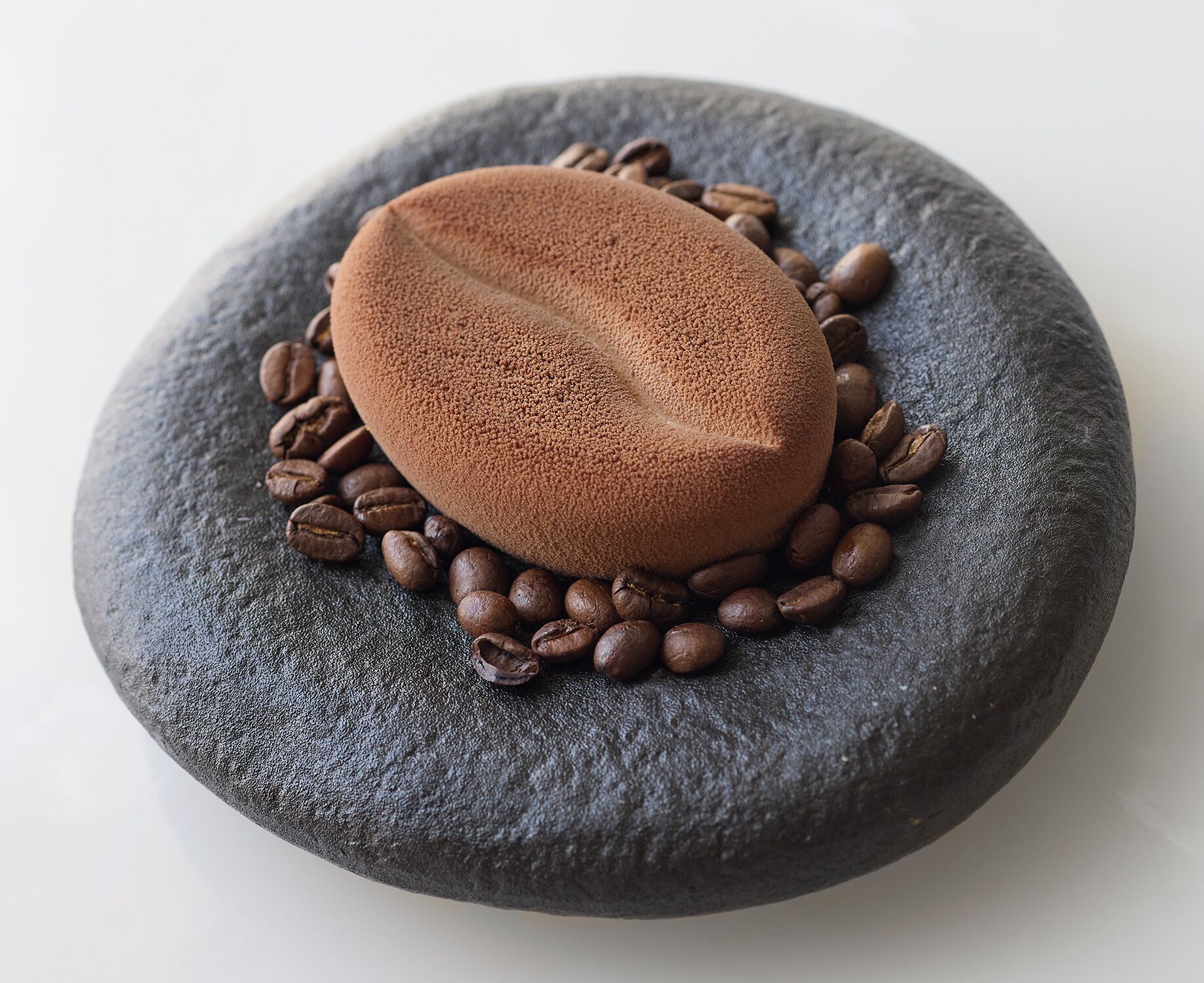 Uma pedra arredondada com um objeto liso e em formato de oval sobre ela, cercada por grãos de café espalhados.