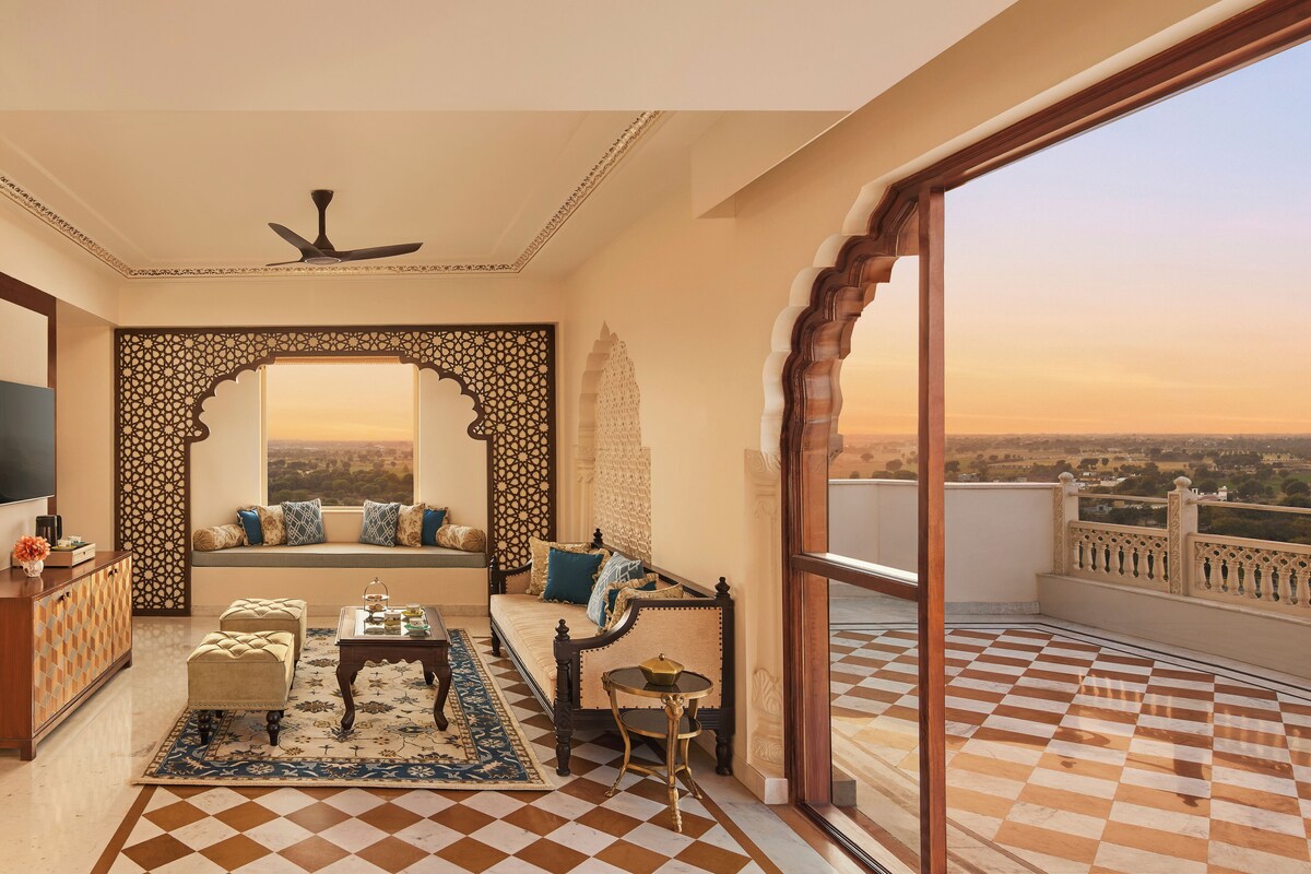 A balcony with a checkered floor, a sofa with cushions, a small table, and a decorative screen.