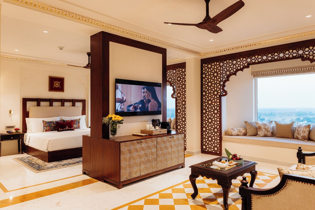 A hotel room with a bed, a TV, a sofa, a coffee table, and a decorative wall.