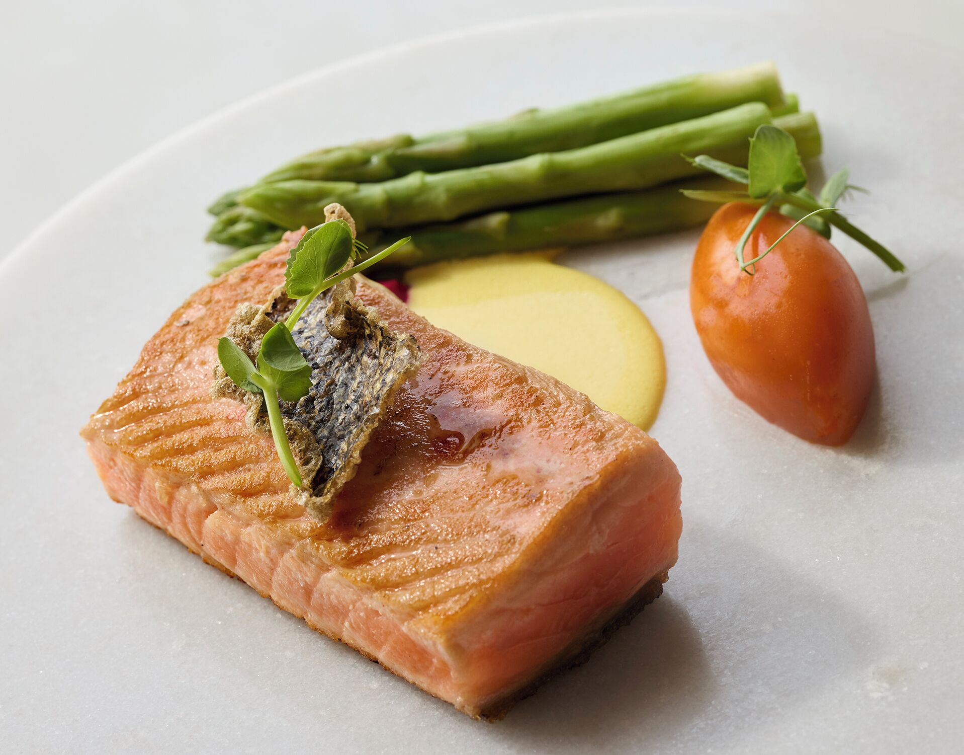Un plato con salmón, espárragos, tomate y una rodaja de limón.