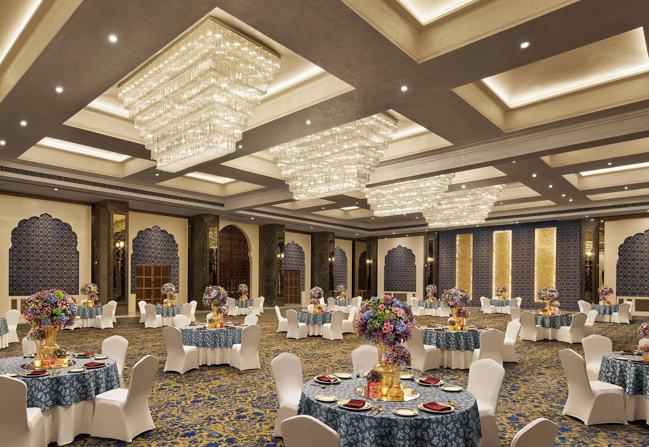 Un salón de banquetes con mesas redondas, sillas blancas y candelabros.