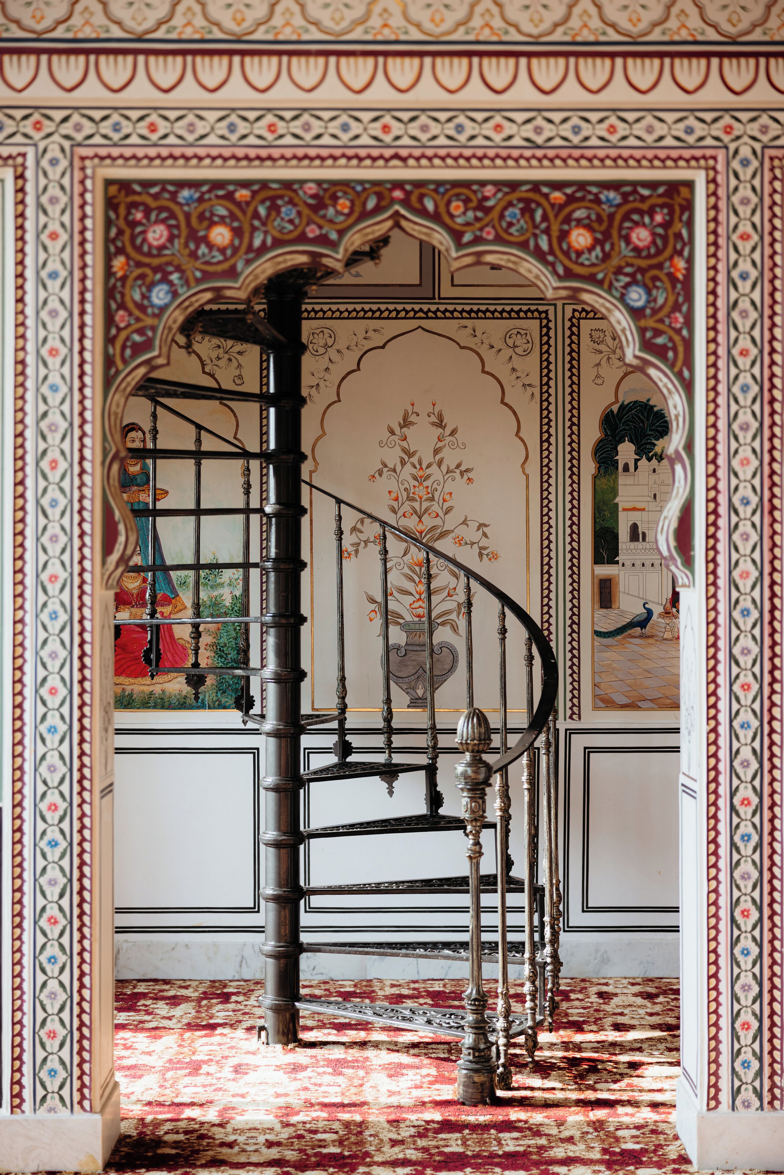 Un escalier en colimaçon orné de rampes décoratives et recouvert d’un tapis à motifs.
