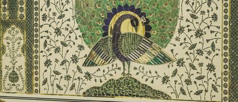 Una habitación con un mosaico de pavo real en la pared, un sofá tapizado en azul y una mesa redonda con base dorada.