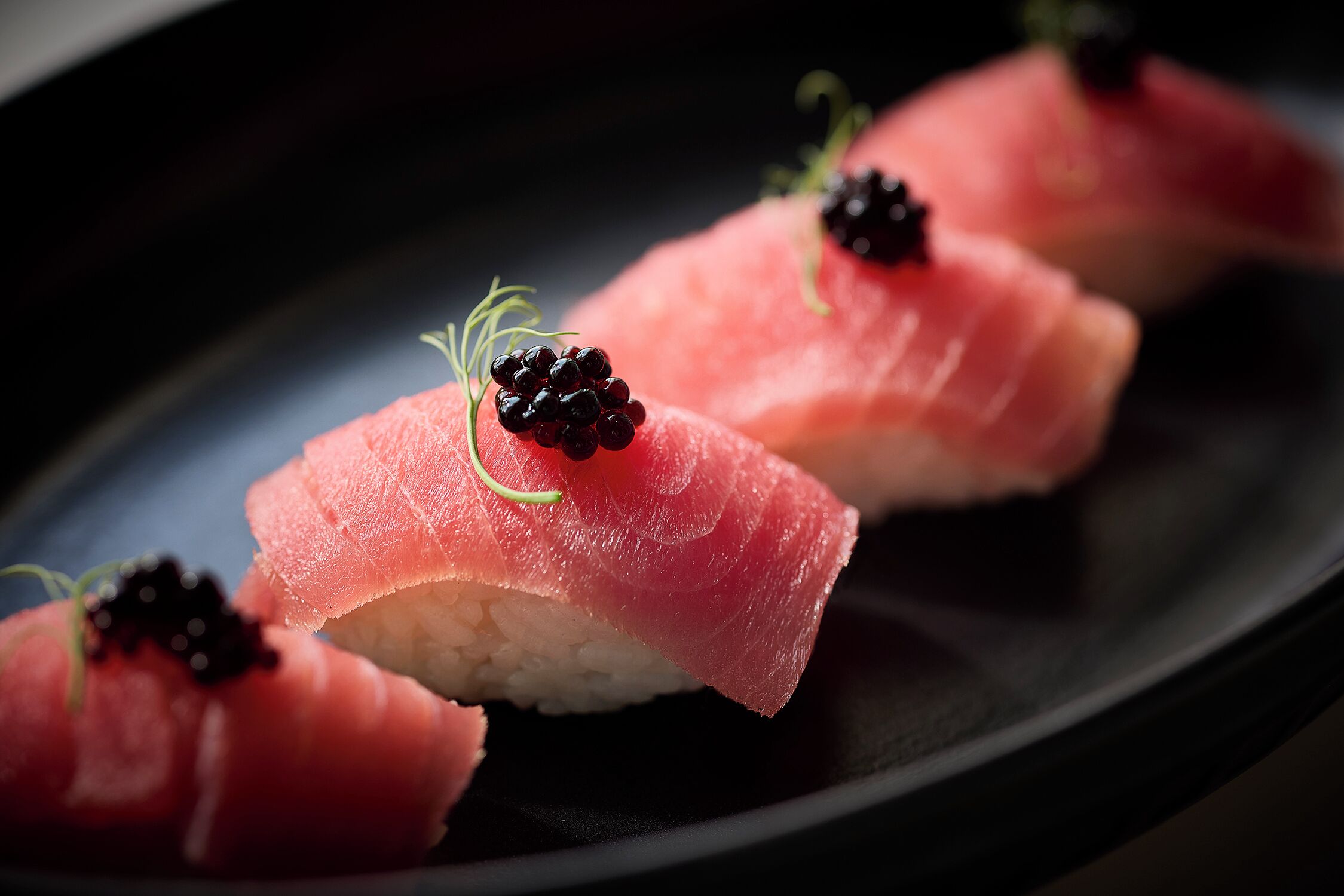 Three pieces of sushi with salmon and black caviar on a dark plate.