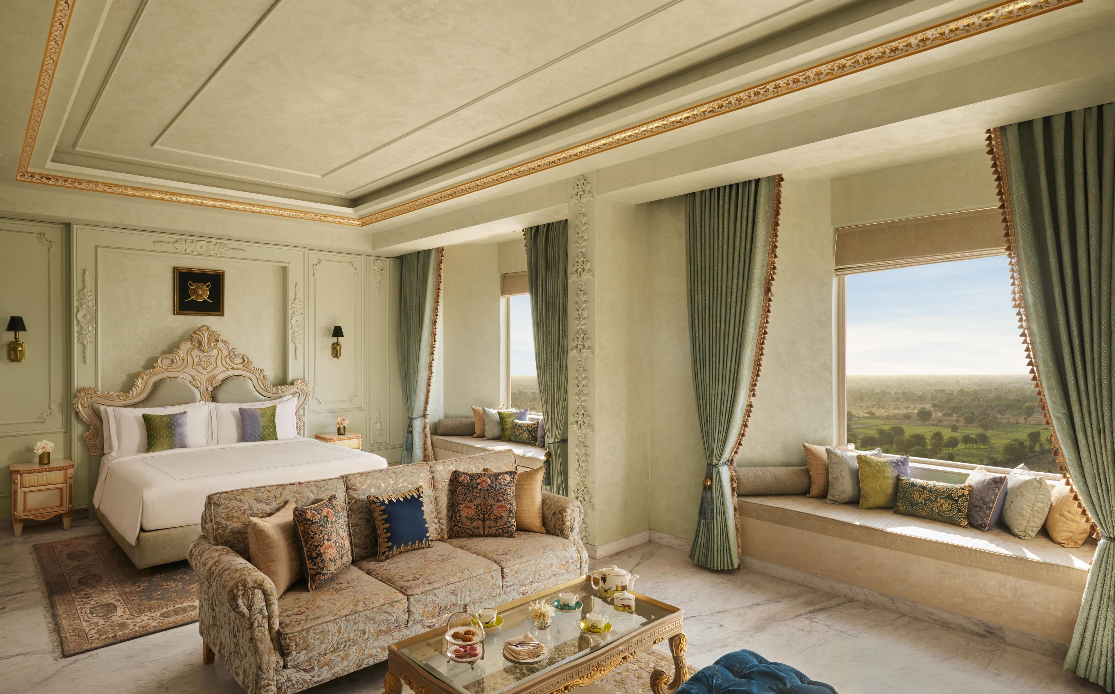 A luxurious bedroom with a large bed, a sofa, a glass coffee table, and a view of the countryside.