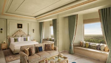 A luxurious bedroom with a large bed, a sofa, a glass coffee table, and a view of the countryside.