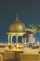 Vista nocturna de un pabellón tradicional con cúpula y arcos, rodeado de mesas y sillas, probablemente parte de un hotel o complejo turístico.