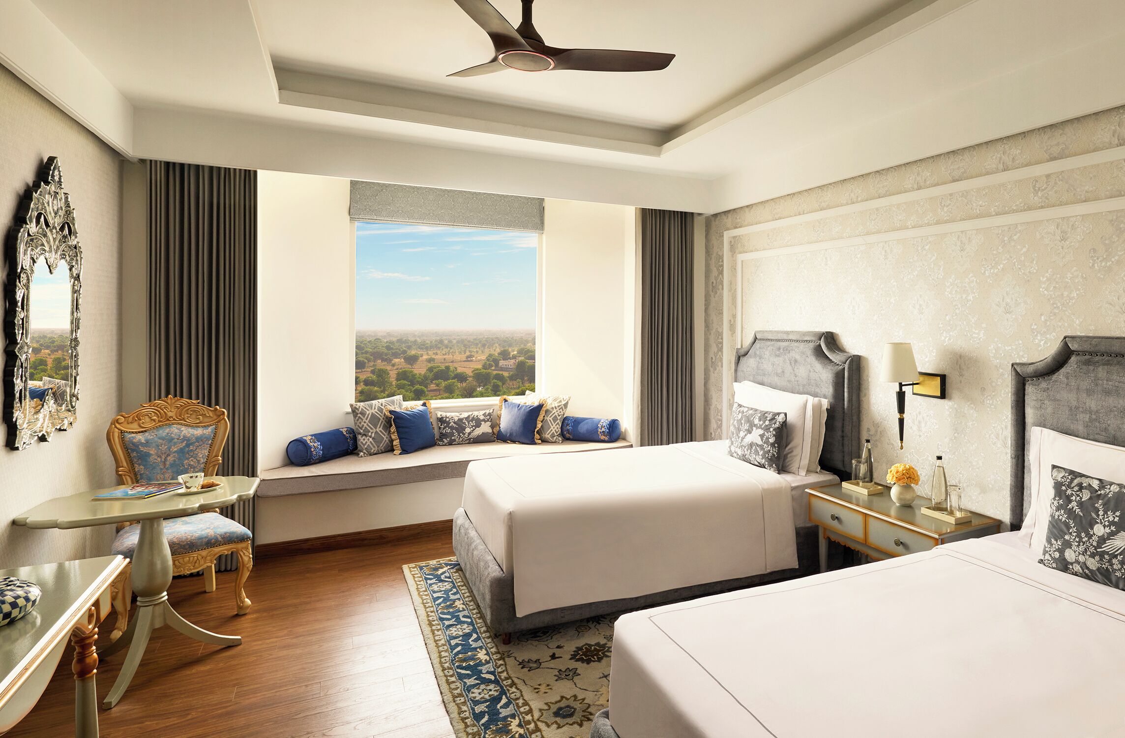 A hotel room with a large bed, a smaller bed, a seating area with a view, a desk, and a ceiling fan.