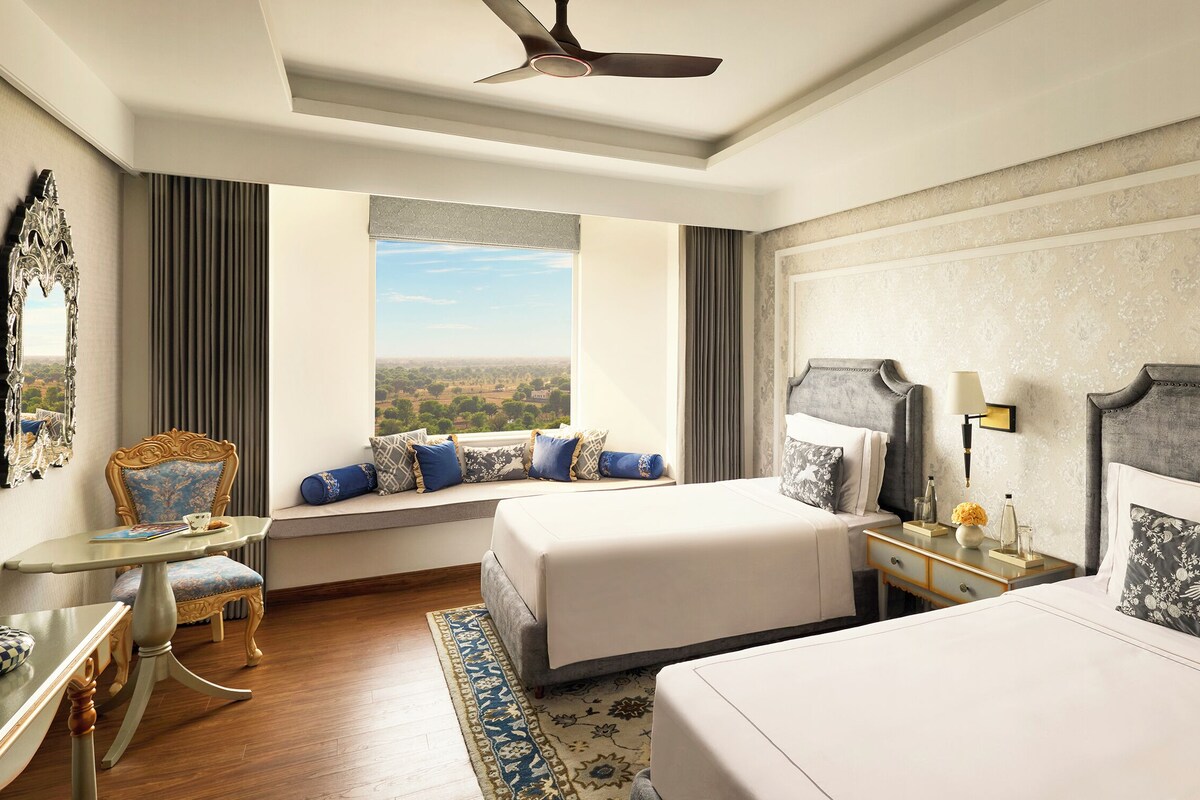 A hotel room with a large bed, a smaller bed, a seating area with a view, a desk, and a ceiling fan.