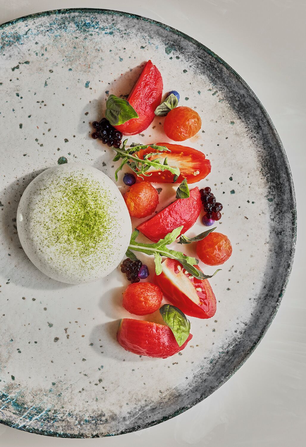A dessert plate with a scoop of white ice cream topped with green matcha powder, accompanied by sliced strawberries, blueberries, and a sprig of mint.