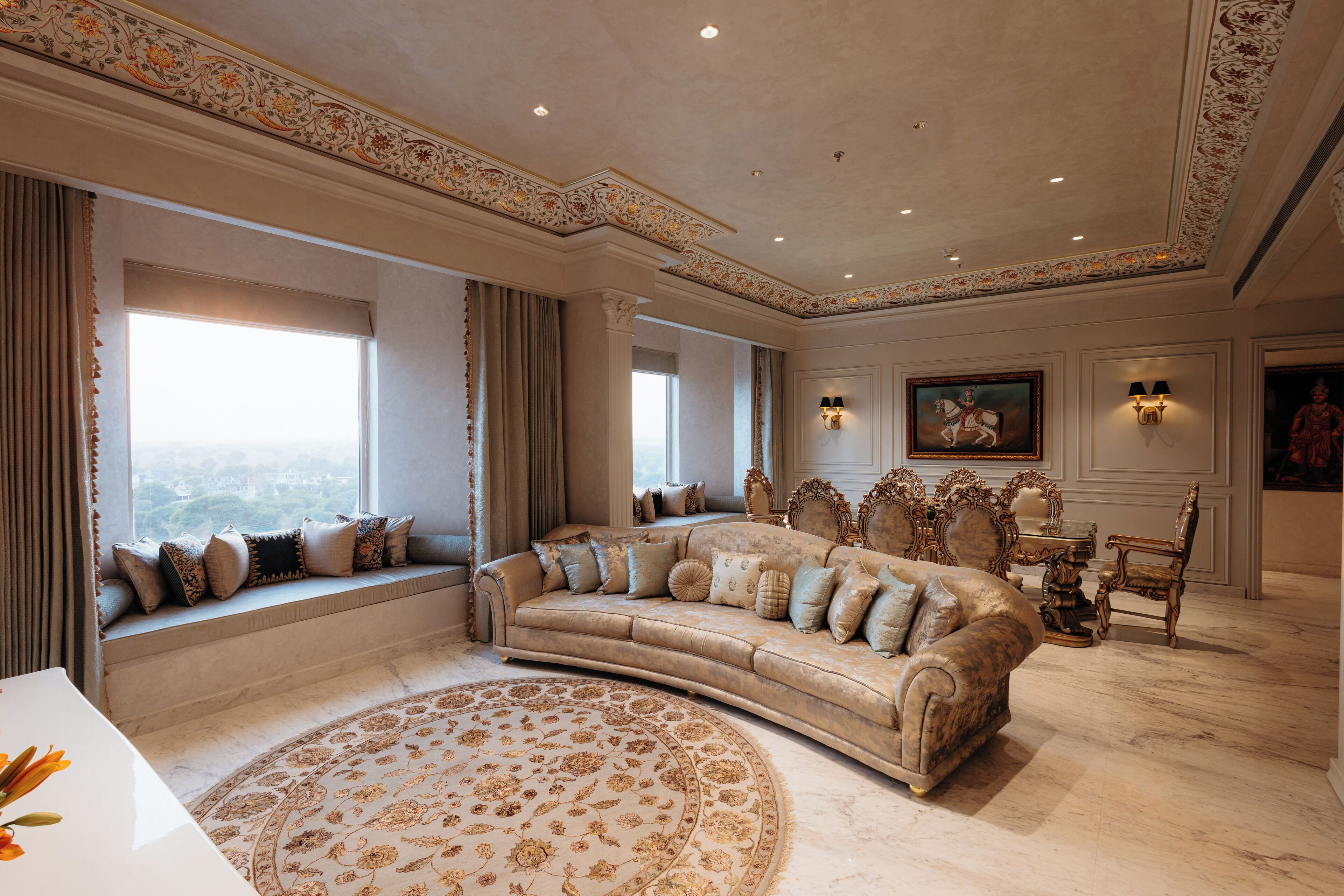 Un salón lujoso con un sofá grande color beige, un tapete redondo estampado y vistas de la ciudad a través de amplias ventanas.