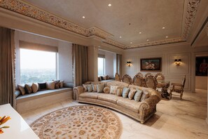 A luxurious living room with a large beige sofa, a round patterned rug, and a view of the city through large windows. - Anantara Jewel Bagh Jaipur (Jaipur)