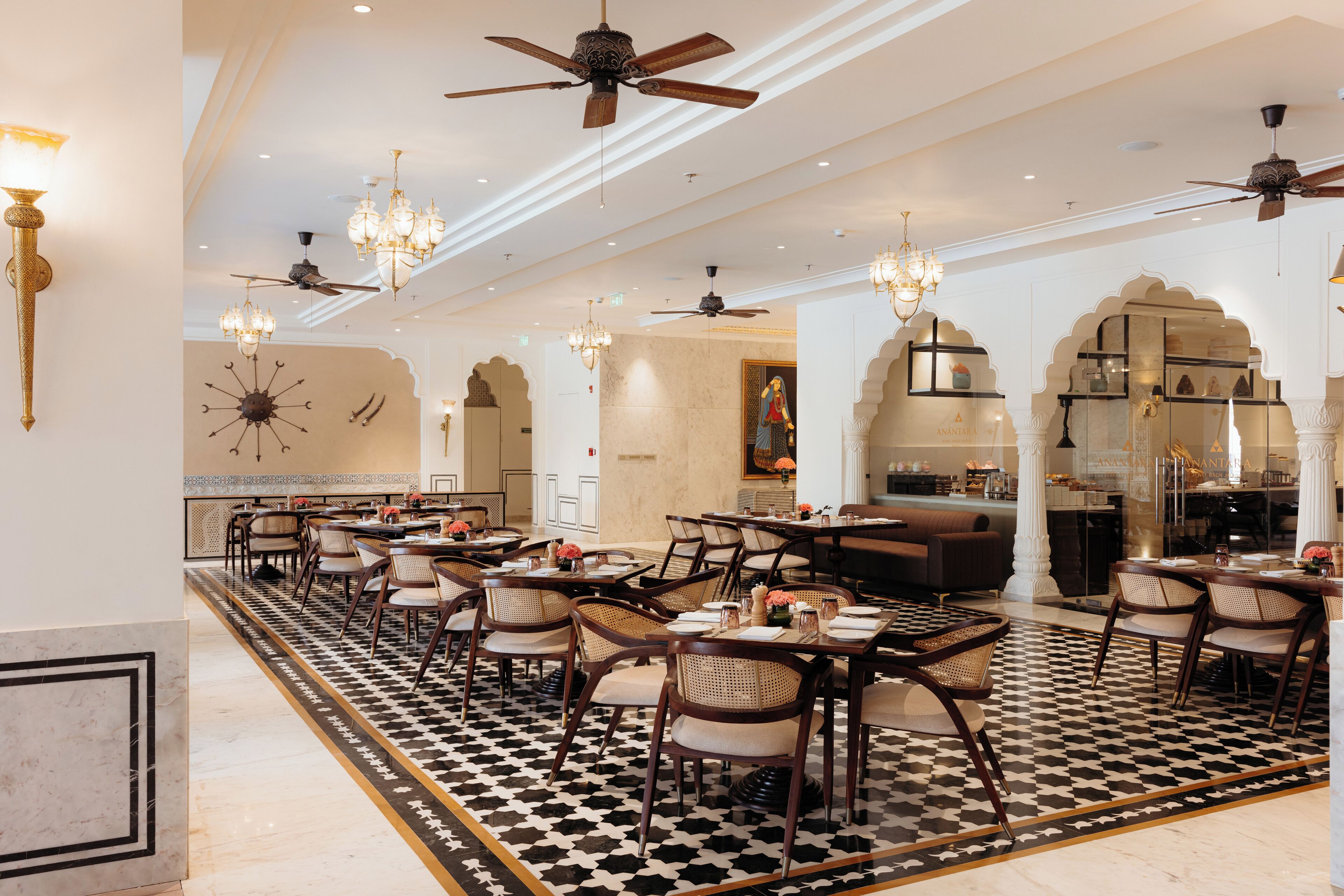 A spacious dining area with multiple tables and chairs, ceiling fans, chandeliers, and a patterned floor.