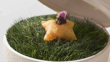 Un bol con superficie texturizada y tapa, que contiene un pastel con forma de estrella sobre un lecho de hierba verde, con una flor decorativa encima.