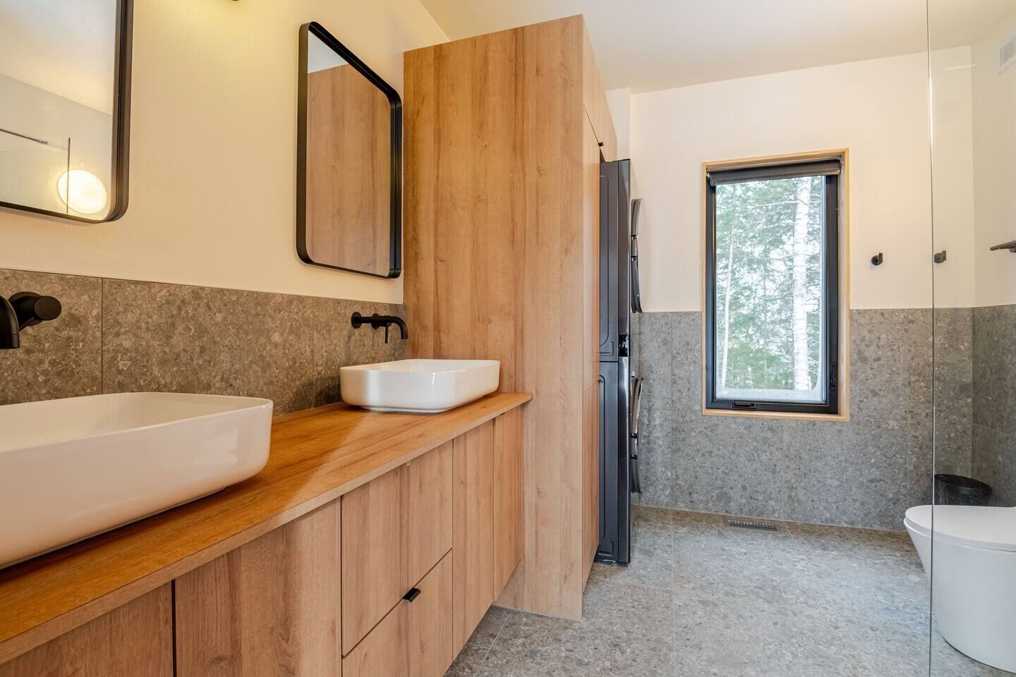 Une salle de bain moderne avec un grand lavabo, un meuble-lavabo en bois, un miroir, une fenêtre et des toilettes.