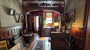 Ein traditionelles Interieur mit Holzvertäfelung, einer Treppe, die zu einem hellerem Raum führt, und einem großen Teppich auf dem Boden.