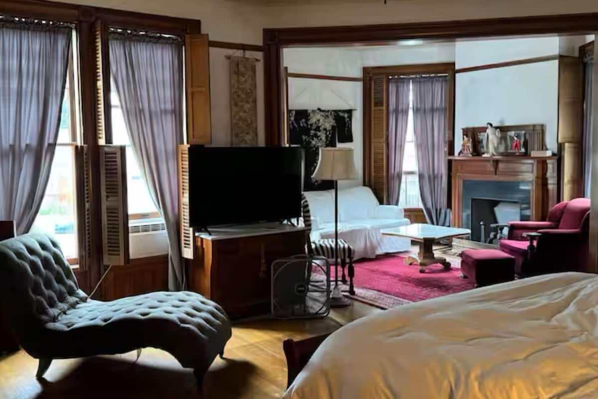 Una habitación de hotel con cama, televisor, escritorio, silla y ventilador de techo.